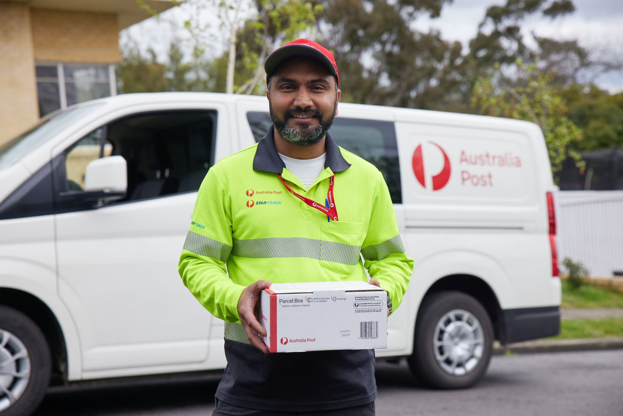 A delivery contractor standing in front of hs van smiling and holding a parcel